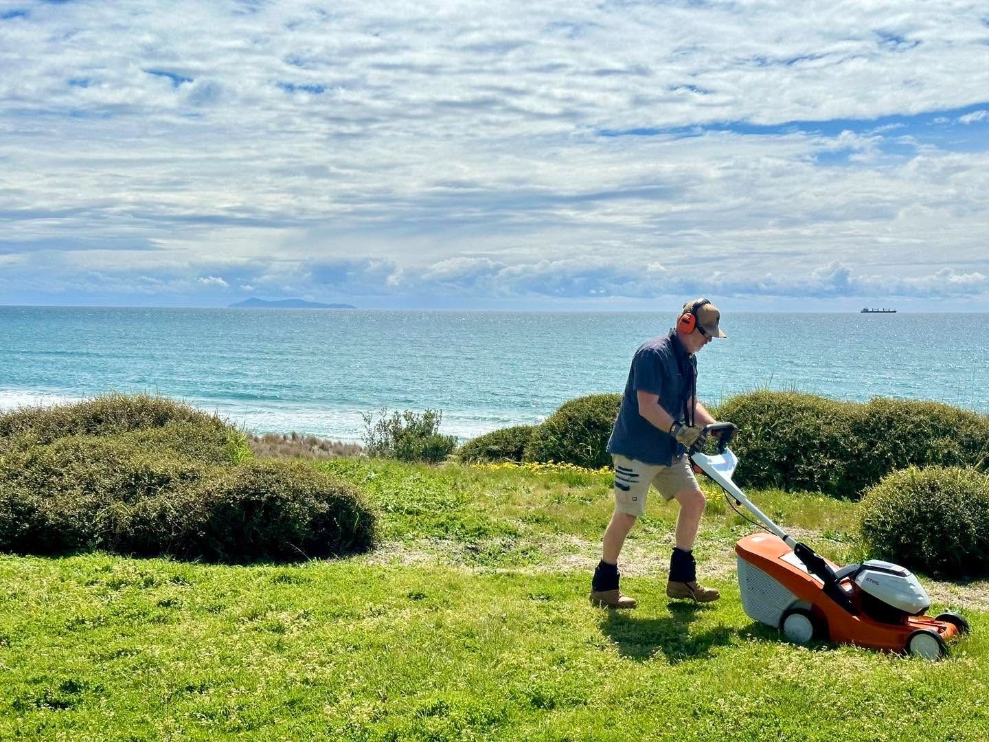 Richard Thurlow of Lawns A Plenty mowing a beachfront lawn overlooking the Bay of Plenty